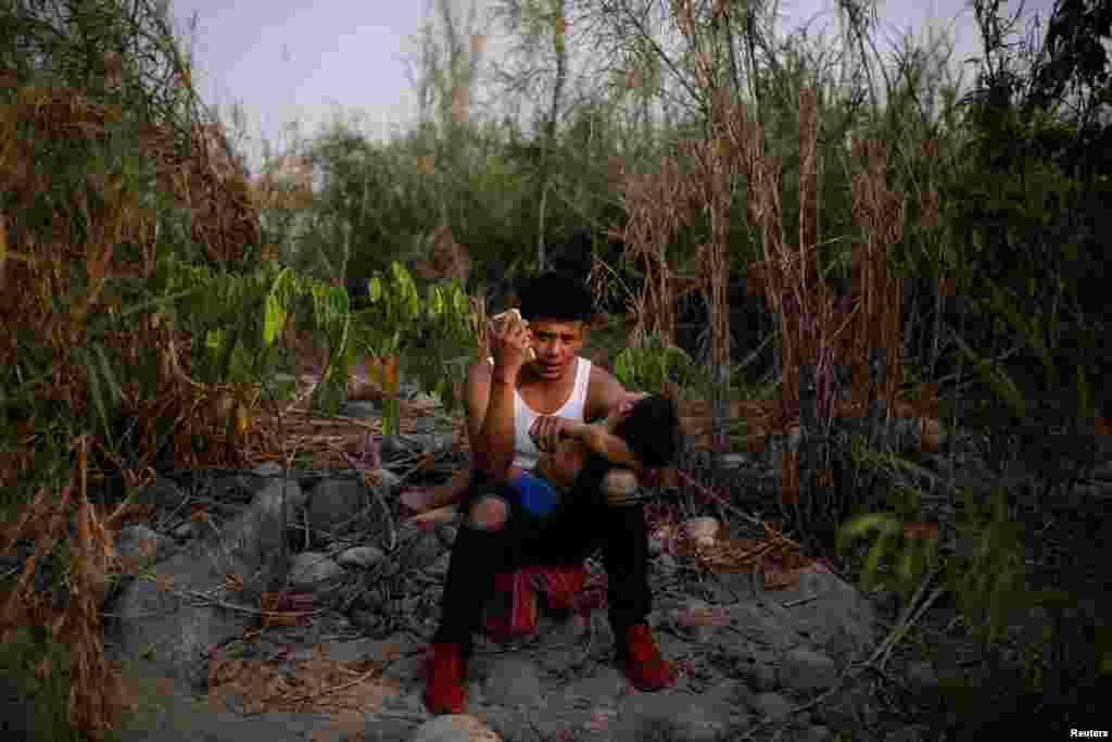 A migrant from Central America talks with his family on his cell phone by a river in Huixtla, Mexico, while taking a break from his journey toward the United States, April 16, 2019.