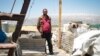 Hussein Muhammed Michel stands among his family's possessions. They have moved the items outside the home in anticipation of a move, but have not yet found a site to move to.