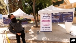 A private security guard gives directions to people looking to get vaccinated, as banners advertise the availability of the Johnson & Johnson and Pfizer COVID-19 vaccines at a county-run vaccination site in Los Angeles on July 22, 2021. 
