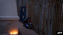 Migrantes miran a través de la valla fronteriza entre Estados Unidos y México, en la frontera entre Estados Unidos y México en Tijuana, estado de Baja California, el 2 de abril de 2021.