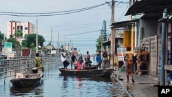 Residents board canoes in a city street flooded by an overflowing drainage canal, in the Saint Martin neighborhood of Cotonou, Benin, 9 Oct 2010