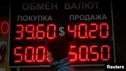 A woman passes by a board showing currency exchange rates in Moscow, Oct. 6, 2014.