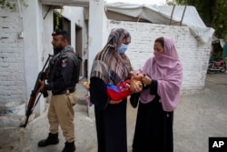 FILE - A police officer stands guard as a health worker, right, administers a polio vaccine to a child in a neighborhood of Peshawar, Pakistan, Sept. 9, 2024.