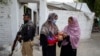 A police officer stands guard as a health worker, right, administers a polio vaccine to a child in a neighborhood of Peshawar, Pakistan, Sept. 9, 2024. 