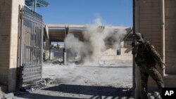 FILE - A member of the U.S.-backed Syrian Democratic Forces, SDF, throws a bomb to check for more explosives as they clear the stadium that was the site of Islamic State fighters' last stand in the city of Raqqa, Syria, Oct. 18, 2017. 