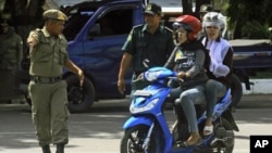 A local security personnel and a Sharia policeman stop women who flout the province's dress code by wearing tight pants during a street inspection in Banda, Aceh, June 9, 2011.