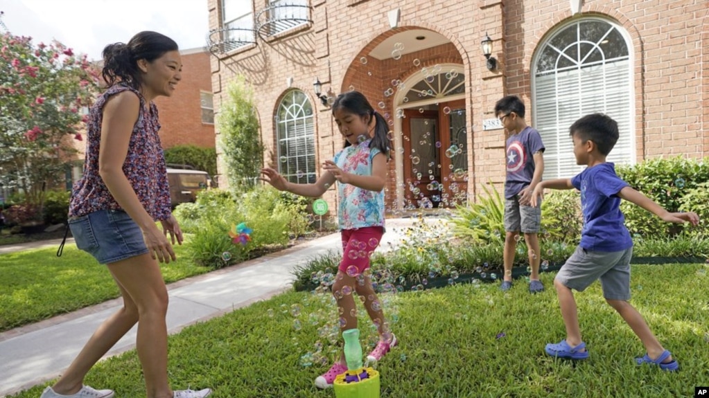 Vicky Li Yip sets up a bubble machine for her children, L to R, Kelsey, 8, Toby, 10 and Jesse, 5, outside their home, July 10, 2020 in Houston. She works from home and says online schooling has been exhausting, even with her husband helping out. (AP Photo/David J. Phillip)