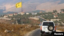 Mobil Penjaga Perdamaian PBB melintas di depan bendera Hizbullah di desa Khiam, perbatasan Lebanon dan Israel, 28 Juli 2020. 