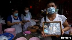 Adulwitch Tangsupmanee, 42, holds up a picture of his father Chanchai Tangsupmanee, who died at age 73 of the coronavirus disease (COVID-19) in July, at his late father's food stall in Bangkok's Chinatown, Thailand, October 6, 2021. (REUTERS/Athit Perawongmetha)