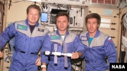 Expedition 1, the first space station crew, poses inside the Zvezda service module with a model of the young International Space Station. Pictured in December 2000 (from left) are Commander William Shepherd and Engineers Yuri Gidzenko and Sergei Krikalev.