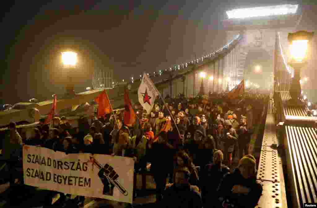 Macaristan’ın başkenti Budapeşte’de yeni çalışma yasasını protesto edenler köprüde yürüyor. Göstericinin taşıdığı dövizin üzerinde “Özgür Ülke, Özgür Üniversite” yazıyor