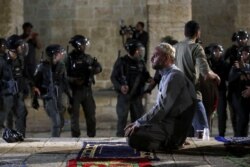 A Palestinian man prays as Israeli police gather during clashes at the compound that houses Al-Aqsa Mosque, known to Muslims as Noble Sanctuary and to Jews as Temple Mount, May 7, 2021.