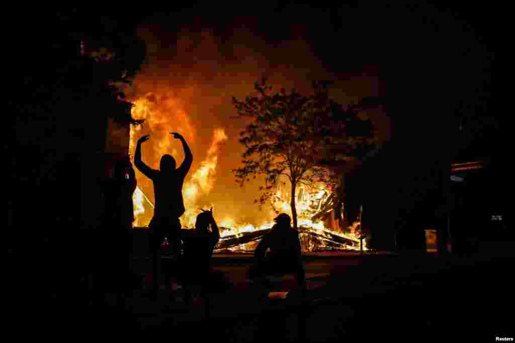 People react as fire rages in the background while protests continue after a white police officer was caught on a bystander&#39;s video pressing his knee into the neck of African-American man.