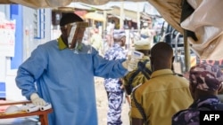 FILE - A medical assistant checks the temperature of people from Democratic Republic of Congo (DRC) at the Ebola screening point bordering with DRC in Mpondwe, western Uganda, on Dec. 12, 2018.