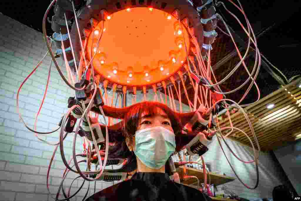 A woman wearing a face mask has her hair curled by a special equipment at a beauty salon in Bangkok, Thailand.