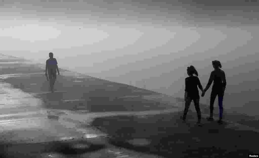 People walk along a foggy embankment of the Yenisei river in the Siberian town of Divnogorsk, Russia.