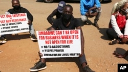 FILE —In this Sept. 14, 2020 file photo, a student and human rights activist holds a banner with others during a peaceful protest in Harare, Zimbabwe. Opposition officials, human rights groups and some analysts accuse the government of abusing the rights of critics. 