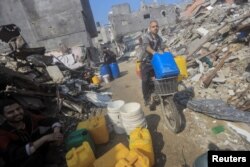 FILE —A man rides a bike with containers as Palestinians collect water from a house destroyed by an Israeli strike, in Jabalia refugee camp in the northern Gaza Strip February 7, 2024.