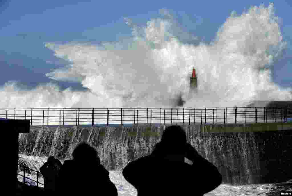 People take pictures of huge waves crash on the Viavelez seafront in the northern Spanish region of Asturias, Spain, Jan. 2, 2016.