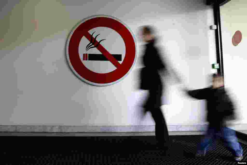 ایک خاتوں اپنے بیٹے کے ساتھ راستے سے گزرتے ہوئے اور ساتھ ہی سگریٹ پینا منع ہے کا نشان آویزاں ہے