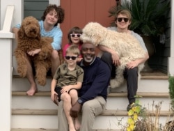 Peter Mutabazi, his children and dogs pose on the steps of their home in Charlotte, North Carolina. He has adopted Anthony, upper left, and he fosters Zay, upper right, and two younger children. (Betty Ayoub/VOA)