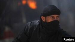 A fighter from the Islamist Syrian rebel group Jabhat al-Nusra in front of a burning vehicle, caused by what activists said were missiles fired by a Syrian Air Force fighter jet in Raqqa province, Syria, May 12, 2013.