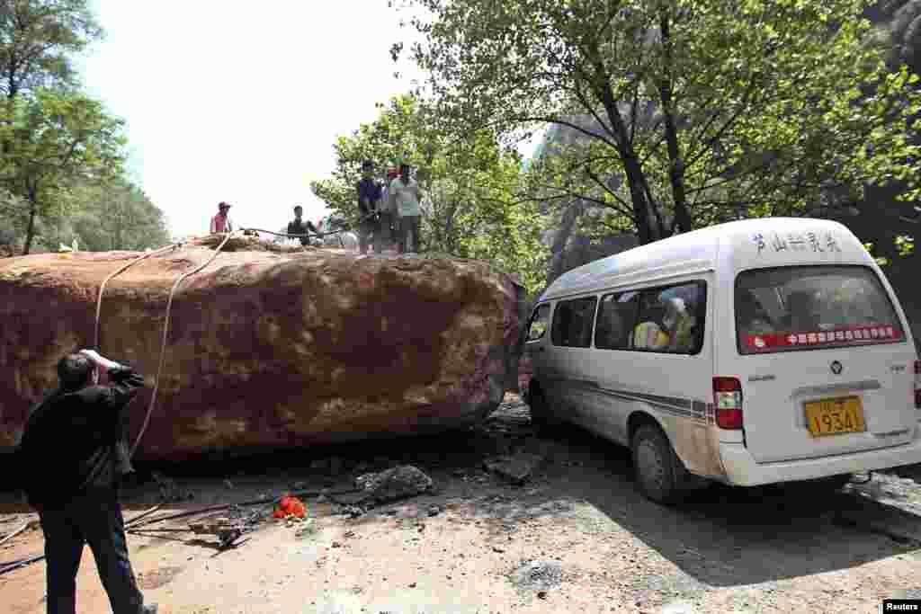 2013年4月20日星期六，中國四川省雅安市蘆山縣發生里氏7級強烈地震。在龍門鄉人們站在一輛被倒塌的大石頭阻擋的車前。