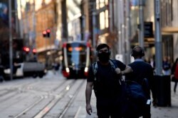 Seorang pria mengenakan masker saat berjalan di sepanjang jalan George di kawasan pusat bisnis Sydney, 25 Juni 2021, di tengah merebaknya varian Delta COVID-19 di negara tersebut. (AFP).