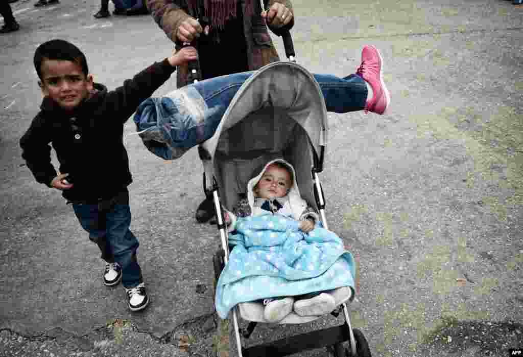 A Syrian woman carries her husband&#39;s prosthetic leg on their baby&#39;s stroller as they arrive with other migrants and asylum seekers to the port of Piraeus, Greece.