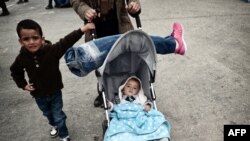 Une syrienne tenant une prothèse de jambe de son mari sur la poussette de leur bébé alors qu'ils arrivent avec d'autres migrants et des demandeurs d'asile vers le port du Pirée, le 21 Octobre 2015.