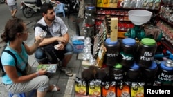 FILE - Tourists try coffee before making purchases at a shop in Hanoi, Aug. 20, 2013.