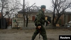 FILE - A member of the self-proclaimed Donetsk People's Republic (DNR) walks past a house damaged by shelling in Donetsk, Ukraine. Putin's purpose in meeting world leaders may be to soften western wrath over its military intervention in Ukraine, analysts said.