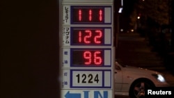 FILE - A car passes behind a board posting oil prices at a service station in Tokyo, Japan, Dec. 16, 2015.