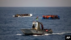 FILE - A Libyan Coast Guard ship sails past two rubber boats packed with migrants and refugees in the Mediterranean Sea, about 18 miles north of Sabratha, Libya, June 15, 2017.