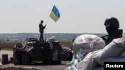 FILE - A Ukrainian soldier raises a Ukrainian flag on top of an armored personnel carrier at a checkpoint near the town of Slovyansk in eastern Ukraine.