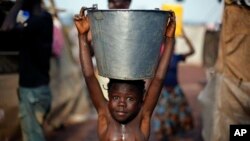 Seorang anak yang membawa ember berisi air berjalan di tengah lumpur menyusul badai yang menyerang kamp pengungsi di bandar udara Bangui, Republik Afrika Tengah (2/2). (AP/Jerome Delay)