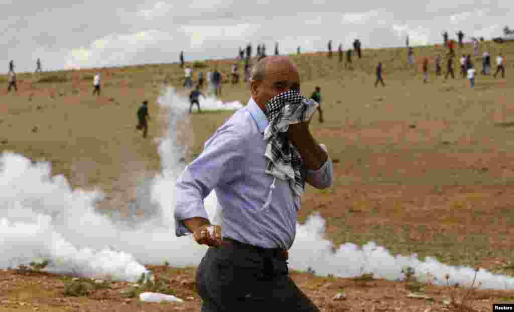 A Turkish Kurd protester runs away from tear gas fired by riot police near the Turkish-Syrian border in the southeastern town of Suruc in Sanliurfa province. 