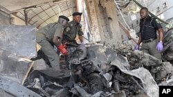 Police anti-bomb officers stand on the burnt engine of the Jeep used by the suicide bomber that ravaged ThisDay Newspapers rocked by bomb explosions killing two security men, the suicide bomber and injuring five of the company's support staff, April 26, 2