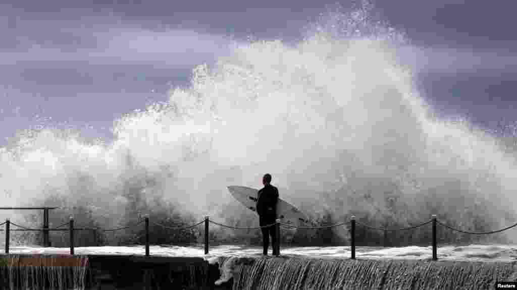 A surfer waits for a break in crashing waves before diving in for a surf off Sydney&#39;s Collaroy Beach. A cyclonic storm lashed Australia&#39;s east coast for a third day on Wednesday, causing millions of dollars of damage to property and infrastructure in Sydney and other cities.