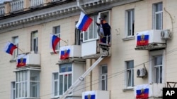  Рабочие устанавливают российские флаги на многоквартирном доме в оккупированном Россией Луганске 27 сентября 2022 (Архивное фото: AP)
 