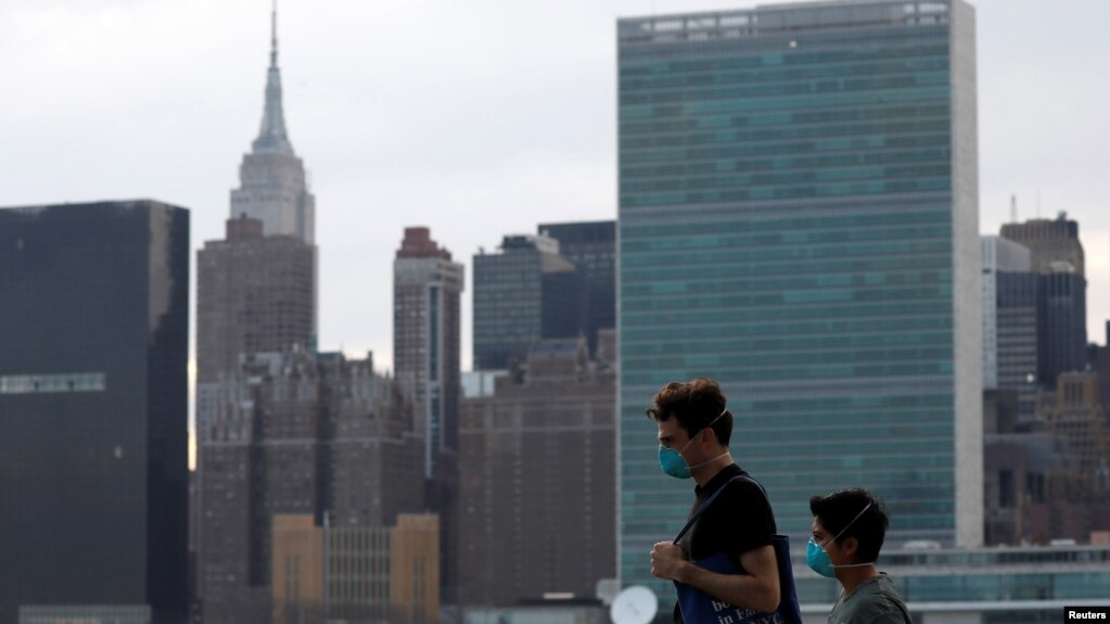 People in protective masks walk in front of the Manhattan skyline along the waterfront of Long Island City as the coronavirus disease (COVID-19) outbreak continues in the Queens borough of New York City, U.S., March 20, 2020. REUTERS/Andrew Kelly