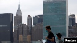 Para pejalan kaki mengenakan masker melintas di depan gedung-gedung di Manhattan, New York, di tengah wabah virus corona, 20 Maret 2020. (Foto: Reuters ) 