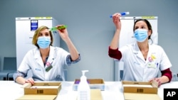 FILE - Health workers inspect vials of the Pfizer-BioNTech COVID-19 vaccine as they are thawed in a lab at the UZ Leuven hospital in Leuven, Belgium, Dec. 27, 2020. 