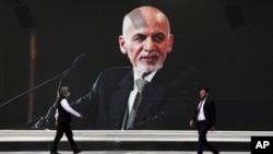 Hombres pasan junto a un mural del presidente Ashraf Ghani en el aeropuerto internacional Hamid Karzai, en Kabul, Afganistán, el 14 de agosto de 2021.