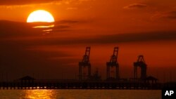 FILE- In this Dec. 2, 2018, file photo cranes at the Port of Gulfport are silhouetted by the setting sun at Gulfport, Mississippi. 