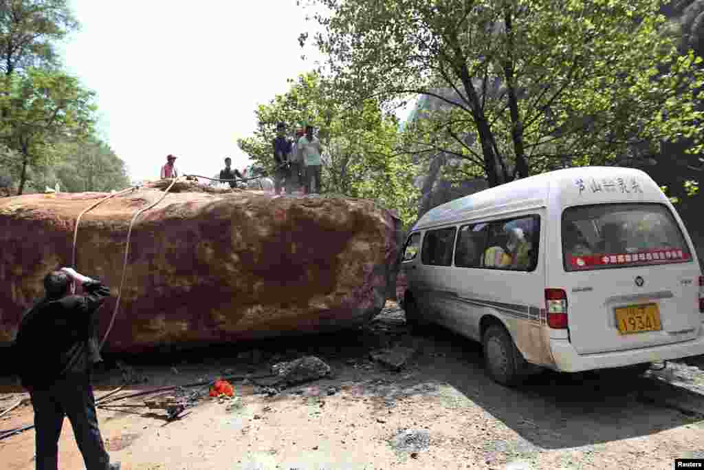 Warga berdiri dekat sebuah mobil van di sebuah jalan yang tertutup batu besar pasca gempa bumi berkekuatan 6.6 yang mengguncang desa Longmen wilayah Lushan, Ya&#39;an, propinsi Sichuan, 20 April 2013.