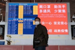 In this March 12, 2020, photo, a man wearing a mask stands near a display board at the Capital International Airport terminal 3 in Beijing.
