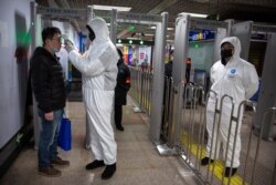 A worker wearing a protective suit takes the temperature of a passenger at the entrance to a subway station in Beijing, China, Jan. 26, 2020.
