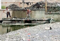 FILE - Workers collect trash from a canal in Beijing, China, June 29, 2004.