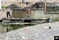 FILE - Workers collect trash from a canal in Beijing, China, June 29, 2004.
